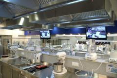 Akademia inspiracji Makro. Widok ze stanowiska kucharza ucznia. Stanowiska kucharzy uczniów, ekrany transmitujące, w dali rząd chłodni. W tym panoramicznym widoku widzimy wszystko to co najważniejsze. Projekt stoiska i nadzór Tatjana Kobuszewska