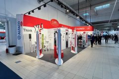 Stoisko targowe z czerwonym brandingiem CAREL i ALFACO oraz hasłem "Think XL". Na stoisku znajdują się panele wystawowe, produkty, stołki i stoły. Obszar jest dobrze oświetlony górnymi światłami; kilka osób stoi i chodzi w pobliżu w dużej, nowoczesnej hali. projekt i nadzór Tatjana Kobuszewska trksystem.com