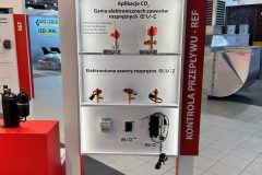 Ekspozycja targowa z brandingiem CAREL przedstawia elektroniczne zawory rozprężne, oznaczone jako "Elektroniczne zawory rozprężne E2V-C" i "E2V-Z", z próbkami produktów zamontowanymi na półkach, ustawionymi w dobrze oświetlonej przemysłowej hali wystawowej. projekt i nadzór Tatjana Kobuszewska trksystem.com