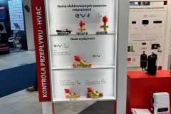 Biało-czerwony stojak z logo CAREL prezentuje różne elektroniczne zawory rozprężne do systemów HVAC. Trzy półki mieszczą metalowe elementy zaworów, a oznakowanie na stojaku jest w języku polskim, podkreślając cechy produktu i efektywność energetyczną. projekt i nadzór Tatjana Kobuszewska trksystem.com