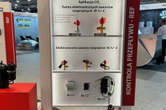 Ekspozycja targowa firmy CAREL prezentuje elektroniczne zawory rozprężne do zastosowań CO₂. Białe stoisko ma czerwone akcenty i półki prezentujące różne modele zaworów, z polskimi etykietami i opisami produktów nad każdym z nich, przy jasnym oświetleniu wystawowym. projekt i nadzór Tatjana Kobuszewska trksystem.com