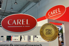 Stoisko targowe z dwoma czerwonymi logotypami CAREL wyświetlanymi powyżej. Na konstrukcji stoiska znajduje się złota tabliczka "PTAK WARSAW EXPO Excellence Award". Poniżej logotypów widoczna jest część polskojęzycznego napisu informacyjnego. Otoczenie to nowoczesna, przemysłowa hala. projekt i nadzór Tatjana Kobuszewska trksystem.com