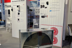 Stoisko targowe z brandingiem CAREL, plakatami informacyjnymi w języku polskim na temat rozwiązań chłodniczych i dużym przemysłowym wentylatorem chłodniczym umieszczonym z przodu. Przestrzeń jest nowoczesna z białymi ścianami, krzesłami i widoczną literaturą produktową. projekt i nadzór Tatjana Kobuszewska trksystem.com