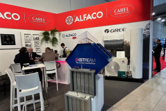 Stoisko targowe z czerwonymi banerami ALFACO i CAREL. Ludzie siedzą przy stolikach po lewej stronie, z broszurami i laptopami. Z przodu eksponowane są metalowe filtry HVAC i niebieski klimatyzator DXSTREAM. W tle widoczne są produkty GREE i duże zdjęcia. projekt i nadzór Tatjana Kobuszewska trksystem.com