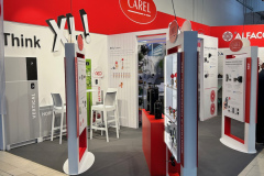 Stoisko targowe z czerwono-białym brandingiem CAREL prezentuje produkty HVAC i panele informacyjne. Dwa białe krzesła i stół są ustawione do spotkań, a nad nimi wiszą światła. Stoisko zawiera próbki produktów i odważne oznakowanie na ścianach. projekt i nadzór Tatjana Kobuszewska trksystem.com