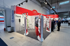 Czerwono-białe stoisko targowe prezentuje marki ALFAKO i CAREL. Na stoisku znajdują się panele produktowe, półki i stojaki informacyjne. Kilka osób wchodzi w interakcje w pobliżu stoiska, które jest ustawione w przestronnej, dobrze oświetlonej hali wystawowej. projekt i nadzór Tatjana Kobuszewska trksystem.com