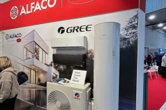 Stoisko targowe prezentuje logo ALFACO i CAREL na czerwonym znaku nad urządzeniami grzewczo-chłodzącymi GREE, w tym jednostką zewnętrzną, podgrzewaczem wody i broszurami. W pobliżu znajdują się ludzie, a część nowoczesnego budynku zdobi stoisko. projekt i nadzór Tatjana Kobuszewska trksystem.com