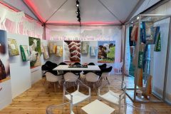 Nowoczesne stoisko Stoisko reklamowe Dolfos z wystrojem o tematyce zwierzęcej, przezroczystymi i białymi krzesłami, małymi stolikami, torbami z produktami na ścianach i kolorowymi opakowaniami karmy dla zwierząt. Drewniana podłoga i pośrednie różowe oświetlenie tworzą przyjazną atmosferę. projekt i nadzór Tatjana Kobuszewska trksystem.com