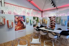 Stoisko reklamowe Dolfos obejmuje przezroczyste krzesła, stół, worki z karmą dla zwierząt umieszczone na ścianach oraz baner z kurczakiem. Stoisko ma drewnianą podłogę, biały baldachim i czerwone oświetlenie akcentujące wzdłuż sufitu. projekt i nadzór Tatjana Kobuszewska trksystem.com