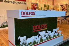 Stoisko reklamowe Dolfos ma ladę z zieloną sztuczną trawą, białe figurki zwierząt i branding firmy. Stoisko eksponuje opakowania produktów, a na ścianach znajdują się ilustracje zwierząt. projekt i nadzór Tatjana Kobuszewska trksystem.com