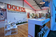 Nowoczesne Stoisko reklamowe Dolfos wyróżnia się dużymi czerwonymi literami na tylnej ścianie, ozdobionymi wizerunkami zwierząt i produktów żywieniowych, a także białą ladą, półkami i drewnianą podłogą wewnątrz namiotu. projekt i nadzór Tatjana Kobuszewska trksystem.com