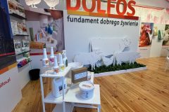 Stoisko reklamowe Dolfos wyróżnia się pogrubionym napisem "DOLFOS fundament dobrego żywienia", ilustracjami zwierząt oraz półkami z produktami weterynaryjnymi i żywieniowymi. Drewniana podłoga dopełnia zachęcającą przestrzeń pod dużym namiotem. projekt i nadzór Tatjana Kobuszewska trksystem.com