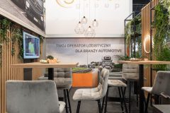 Stoisko targowe na Ptak Warsaw Expo z wysokimi stołami i krzesłami, dużym napisem Global Group, zielenią i ekranem wyświetlającym obrazy; nacisk na nowoczesny wystrój o tematyce motoryzacyjnej w stoisku targowym Global Motion. projekt i nadzór Tatjana Kobuszewska trksystem.com