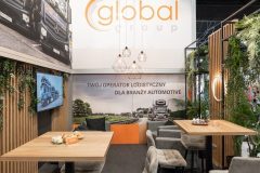 Stoisko targowe Global Motion w Ptak Warsaw Expo to wysokie stoły, szare krzesła, ekspozytory na ścianach ciężarówek, akcenty zieleni i duży znak Global Group z polskim hasłem na tylnej ścianie. projekt i nadzór Tatjana Kobuszewska trksystem.com