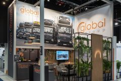 Stoisko targowe Global Motion w Ptak Warsaw Expo wyróżnia się efektownymi zdjęciami ciężarówek, przytulną częścią wypoczynkową, drewnianymi i metalowymi elementami dekoracyjnymi, bujną roślinnością oraz widocznym brandingiem firmy na ścianach i oznakowaniu. projekt i nadzór Tatjana Kobuszewska trksystem.com