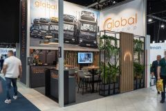 Stoisko targowe Global Motion na Ptak Warsaw Expo prezentuje duże zdjęcia pojazdów, efektowne oznakowanie, recepcję, zielone rośliny i monitor, a po hali wystawowej przechodzą zwiedzający. projekt i nadzór Tatjana Kobuszewska trksystem.com