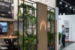 Stoisko targowe Global Motion z przyciągającym wzrok oznakowaniem, bujną roślinnością, nowoczesnymi siedzeniami i panelami działowymi ustawionymi w tętniącej życiem hali Ptak Warsaw Expo z uczestnikami w pobliżu. projekt i nadzór Tatjana Kobuszewska trksystem.com