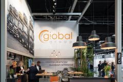 Stoisko wystawiennicze Global Group, pod marką Stoisko targowe Global Motion, z miejscem do siedzenia, wyświetlaczami i rozmawiającymi ludźmi, ustawione w dużej przestrzeni targowej Ptak Warsaw Expo. projekt i nadzór Tatjana Kobuszewska trksystem.com
