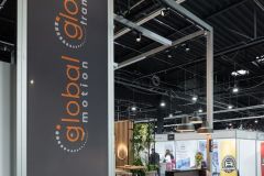 Stoisko targowe Global Motion z dużym pionowym znakiem, ladą i powierzchnią ekspozycyjną, prezentowane w nowoczesnej przestrzeni wewnętrznej w Ptak Warsaw Expo. projekt i nadzór Tatjana Kobuszewska trksystem.com