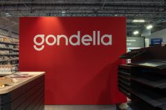 Czerwona ściana w stoisku targowym Gondella w Hali EXPO XXI wyświetla słowo "gondella" pogrubionymi białymi literami, z regałami i ekspozytorami produktów w pobliżu podczas targów Targi Retail Show. projekt i nadzór Tatjana Kobuszewska trksystem.com