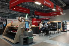 Stoisko targowe Gondella na Hali EXPO XXI podczas targów Retail Show: ekspozycja regałów, strefa z miejscami siedzącymi i banery promocyjne pod industrialnym sufitem. projekt i nadzór Tatjana Kobuszewska trksystem.com