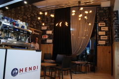 Nowoczesne wnętrze kawiarni na stoisku targowym z ekspresem do kawy, pustymi stolikami i krzesłami, żyrandolem i ścianą z logo różnych marek tworzy atmosferę Fine Dine . warsawsweettech.com . projekt i nadzór Tatjana Kobuszewska trksystem.com