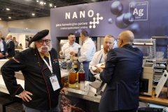 Szef kuchni pozuje w pobliżu ekspozycji kuchennej w Expo XXI podczas Forum Szefów Kuchni i Restauratorów, podczas gdy kilka osób próbuje jedzenia i rozmawia przed stoiskiem promującym nano piece konwekcyjne. projekt i nadzór Tatjana Kobuszewska trksystem.com