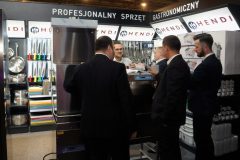 Pięciu mężczyzn w garniturach stoi wokół komercyjnego urządzenia kuchennego Hendi na stoisku Forum Szefów Kuchni i Restauracji na targach Expo XXI, prezentując różne narzędzia i sprzęt kuchenny. projekt i nadzór Tatjana Kobuszewska trksystem.com