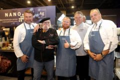 Pięciu mężczyzn, czterech w białych kucharskich uniformach i fartuchach oraz jeden w czarnym kucharskim płaszczu i berecie, pozują razem i uśmiechają się do siebie na Forum Szefów Kuchni i restauratorów w Expo XXI. projekt i nadzór Tatjana Kobuszewska trksystem.com