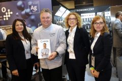 Cztery osoby pozują wewnątrz Expo XXI; jeden mężczyzna w fartuchu szefa kuchni, prawdopodobnie z Hendi, trzyma broszurę, podczas gdy trzy kobiety w strojach biznesowych stoją obok niego podczas Forum Szefów Kuchni i restauratorów. projekt i nadzór Tatjana Kobuszewska trksystem.com