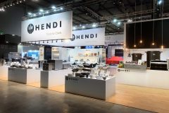 Nowoczesne stoisko targowe dla Hendi z brandingiem Tools for Chefs. Dobrze oświetlona ekspozycja zawiera przybory kuchenne, urządzenia nablatowe i przybory kuchenne na białych stojakach, z górnymi znakami i oświetleniem wiszącym nad podłogą o wzorze drewna. projekt i nadzór Tatjana Kobuszewska trksystem.com