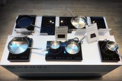 Na nowoczesnej, czarnej płycie indukcyjnej znajduje się sześć patelni i rondli ze stali nierdzewnej. Każda płyta posiada cyfrowy panel sterowania. Pomiędzy patelniami umieszczono znaki informacyjne. Konfiguracja znajduje się na podłodze z jasnego drewna. projekt i nadzór Tatjana Kobuszewska trksystem.com