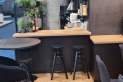 Nowoczesne wnętrze kawiarni z drewnianą podłogą w jodełkę, czarnymi stołkami przy drewnianej ladzie, wiszącymi lampami wiszącymi i roślinami doniczkowymi dodającymi zieleni do przestrzeni. projekt i nadzór Tatjana Kobuszewska trksystem.com