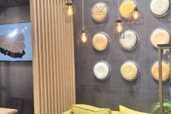 Nowoczesne stoisko targowe firmy Plant-Tec Europe z żółtą sofą, okrągłymi stołami, wiszącymi lampami wiszącymi, dekoracyjnymi płytami ściennymi i napisem "Custom-made Solutions" wyświetlanym na szarej ścianie. projekt i nadzór Tatjana Kobuszewska trksystem.com