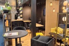 Nowoczesne stoisko wystawowe firmy Plant-Tec z czarno-żółtymi meblami, wzorzystą podłogą, górnym oświetleniem i dużym podświetlanym logo. Rośliny i broszury są wyświetlane na stołach, a na tylnej ścianie znajduje się ekran. projekt i nadzór Tatjana Kobuszewska trksystem.com