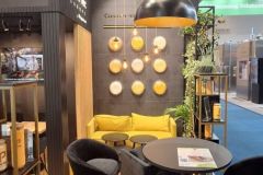 Nowoczesne stoisko targowe z żółtą kanapą, czarnymi krzesłami, okrągłymi stołami, dekoracyjnymi płytami ściennymi i lampami wiszącymi. Stoisko zawiera branding "Paradise" i oznakowanie rozwiązań do przetwarzania żywności. projekt i nadzór Tatjana Kobuszewska trksystem.com