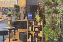 Stoisko targowe firmy Plant-Tech Europe z czarnymi meblami, półkami z produktami roślinnymi i różnymi zielonymi roślinami ułożonymi dekoracyjnie na tle z logo firmy. projekt i nadzór Tatjana Kobuszewska trksystem.com