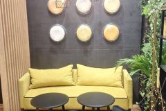 Nowoczesny salon z żółtą sofą, czarnymi stolikami i geometrycznymi lampami wiszącymi. Okrągła grafika ścienna i zieleń zdobią ciemną ścianę pod napisem Custom-made Solutions. projekt i nadzór Tatjana Kobuszewska trksystem.com