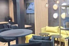 Nowoczesne stoisko targowe dla Plant-Tec Europe z czarno-żółtym wystrojem, wysokimi stołami i krzesłami, geometrycznym oświetleniem, ekspozycją ścienną z talerzami i małą sofą na drewnianej podłodze. projekt i nadzór Tatjana Kobuszewska trksystem.com