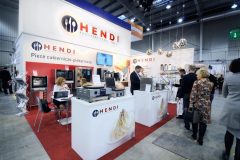 Stoisko wystawowe Hendi, firmy produkującej sprzęt gastronomiczny, z ludźmi wchodzącymi w interakcje handlowcami . urządzenia kuchenne  w jasnym oświetleniu. Korzenie sukcesu dla handlowców, gdy odwiedzający tłoczą się przy stoisku się w hali targowej. projekt i nadzór Tatjana Kobuszewska trksystem.com