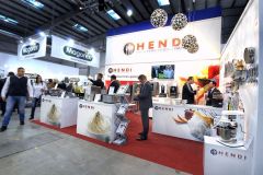 Stoisko targowe prezentuje sprzęt gastronomiczny Hendi na targach Sweet, z personelem angażującym odwiedzających i różnymi urządzeniami kuchennymi prezentowanymi na ladach. projekt i nadzór Tatjana Kobuszewska trksystem.com