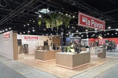 Nowoczesne stoisko wystawiennicze dla La Pavoni z drewnianymi ladami, wystawionymi ekspresami do kawy, wiszącą zielenią i oznakowaniem marki pod oświetleniem sufitowym w dużej wewnętrznej przestrzeni eventowej. projekt i nadzór Tatjana Kobuszewska trksystem.com