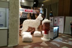 Kryte stoisko reklamowe firmy Bayer obejmuje dużą, białą rzeźbę psa pokrytą sztucznym futrem, kilka pasujących do niej futrzanych stołków, słup ze sztucznego futra oraz automat z piłkami-zabawkami, a wszystko to na tle jesiennych drzew. projekt i nadzór Tatjana Kobuszewska trksystem.com