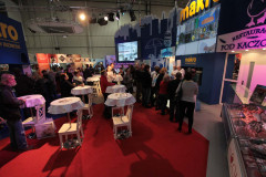 Ludzie gromadzą się i stoją w kolejce na targach wewnętrznych, otoczeni stoiskami takimi jak stoisko targowe Makro CC na targach Eurogastro, z banerami i wysokimi stołami na podłodze wyłożonej czerwonym dywanem. projekt i nadzór Tatjana Kobuszewska trksystem.com