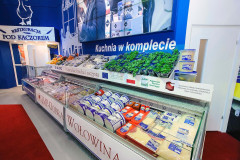 Dział mięsa i produktów w supermarkecie z pakowanym mięsem, warzywami i produktami mlecznymi wystawionymi w lodówkach; polskie znaki i etykiety są widoczne w całym tekście, przypominając stoisko targowe Makro CC w targi Eurogastro. projekt i nadzór Tatjana Kobuszewska trksystem.com