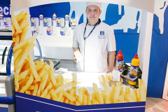 Osoba w mundurze stoi za ladą stoiska gastronomicznego Frytki Express, będącego częścią stoiska targowego Makro CC na targach Eurogastro, ozdobionego wizerunkami frytek i różnych przypraw. projekt i nadzór Tatjana Kobuszewska trksystem.com