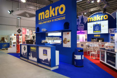 Stoisko wystawiennicze z widocznym stoiskiem targowym Makro CC w kolorze niebieskim i żółtym, z broszurami, materiałami promocyjnymi i miejscem do siedzenia, zlokalizowane na targach Eurogastro w centrum kongresowym. projekt i nadzór Tatjana Kobuszewska trksystem.com