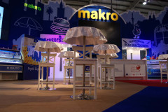 Stoisko targowe Makro CC na targach Eurogastro z makro signage, wysokimi stołami pokrytymi białymi obrusami i różnorodnymi ladami wystawowymi w hali konwencyjnej. projekt i nadzór Tatjana Kobuszewska trksystem.com