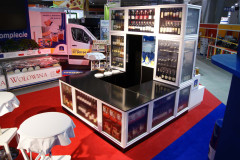 W targi Eurogastro stoi lada wystawowa ze szklanymi gablotami prezentującymi butelki i słoiki; w pobliżu stoiska targowego Makro CC ustawione są stoliki i krzesła. projekt i nadzór Tatjana Kobuszewska trksystem.com