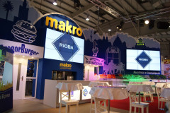 Stoisko wystawiennicze na targach Eurogastro ze stoiskiem targowym Makro CC i marką Rioba, z zadaszonymi stołami i podświetlanymi znakami w dużym pomieszczeniu. projekt i nadzór Tatjana Kobuszewska trksystem.com